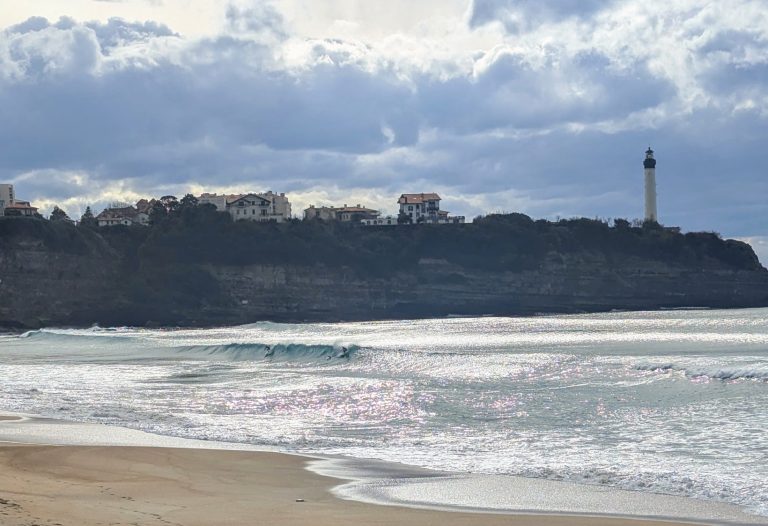 Surfeur à Anglet avec le phare de Biarritz en arrière-plan, symbole du dynamisme et de l’esprit d’équipe au Pays Basque