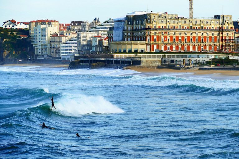 Vue sur l'Hôtel du Palais et la Grande Plage de Biarritz avec des surfeurs, illustrant la culture de l'excellence pour un séminaire d'entreprise.