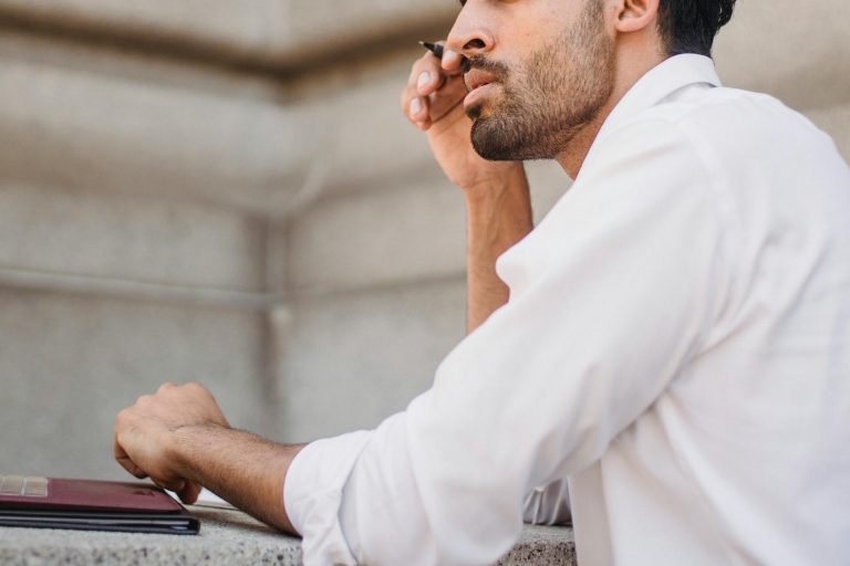 Homme pensif tenant un stylo, symbolisant le désengagement, la dette émotionnelle et le risque de départ d’un collaborateur
