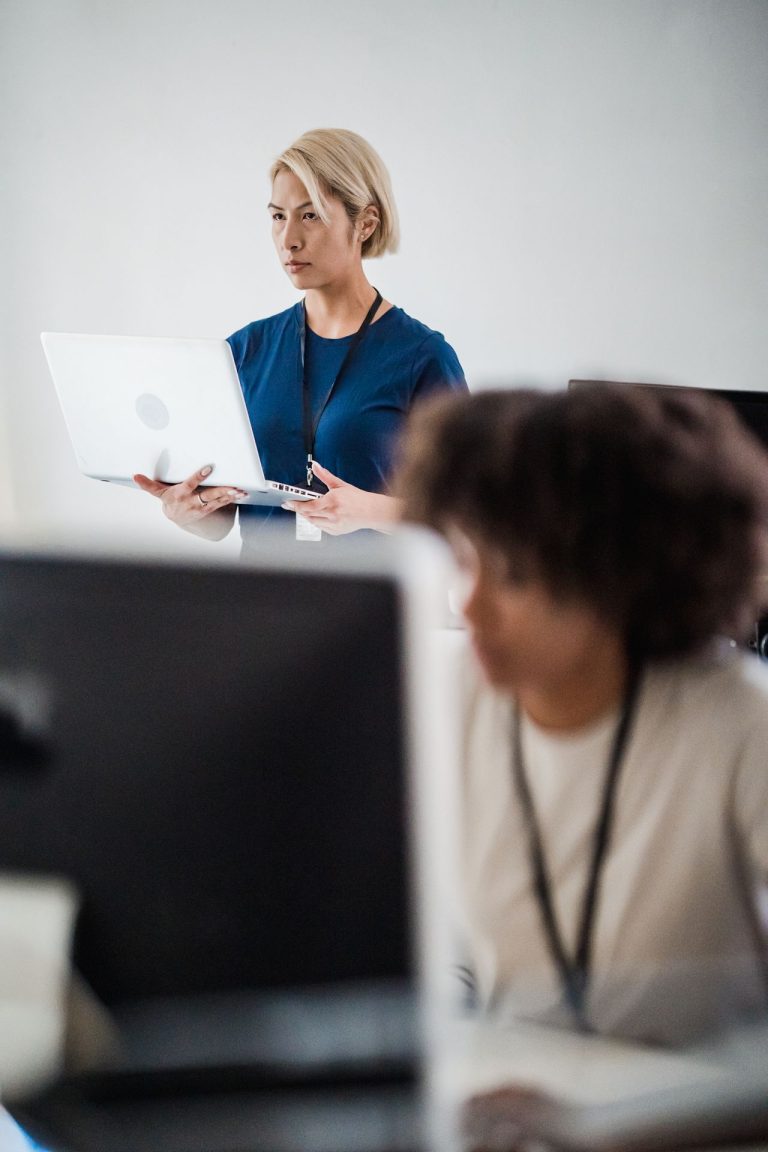 Une dirigeante debout tient son ordinateur portable et observe ses équipes dans un bureau, illustrant le rôle du management et de la prise de décision.