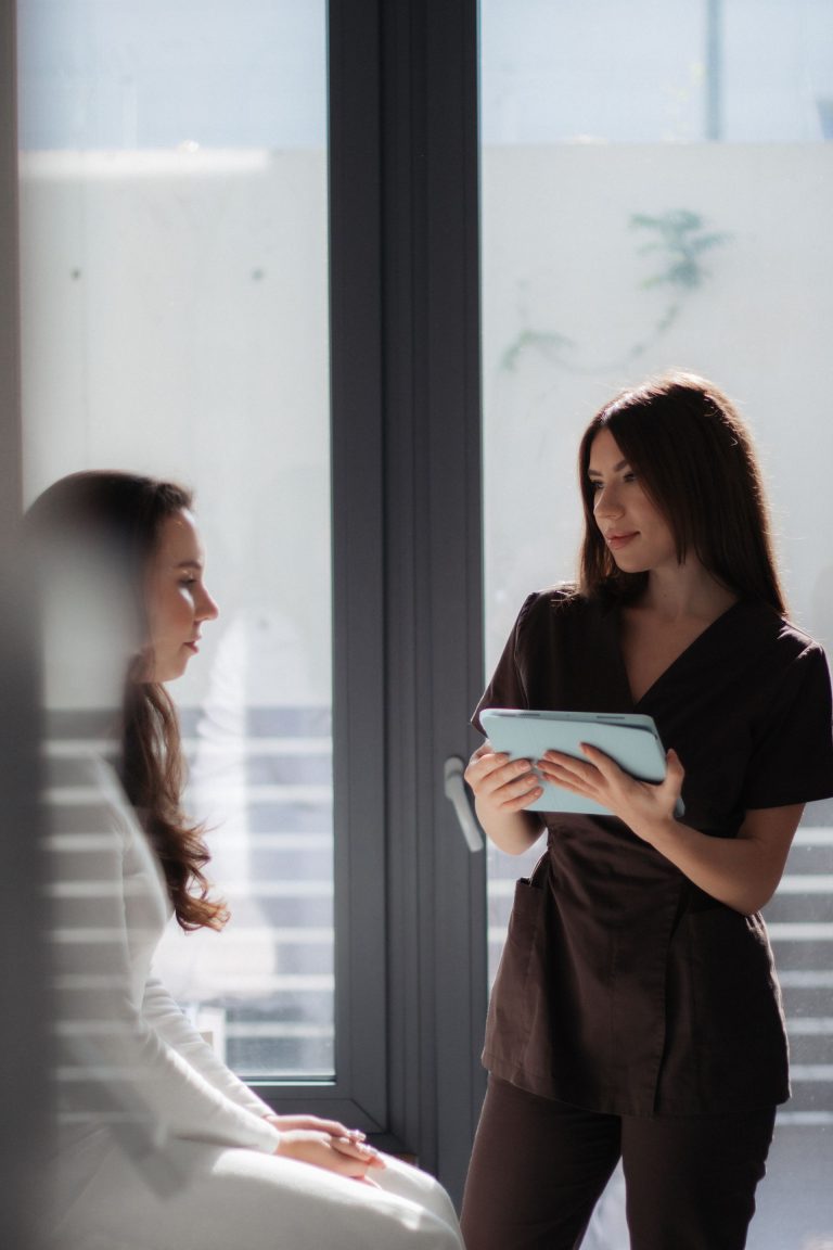 Une manager debout avec une tablette échange avec sa collaboratrice assise pour lui laisser un temps de réflexion avant un entretien
